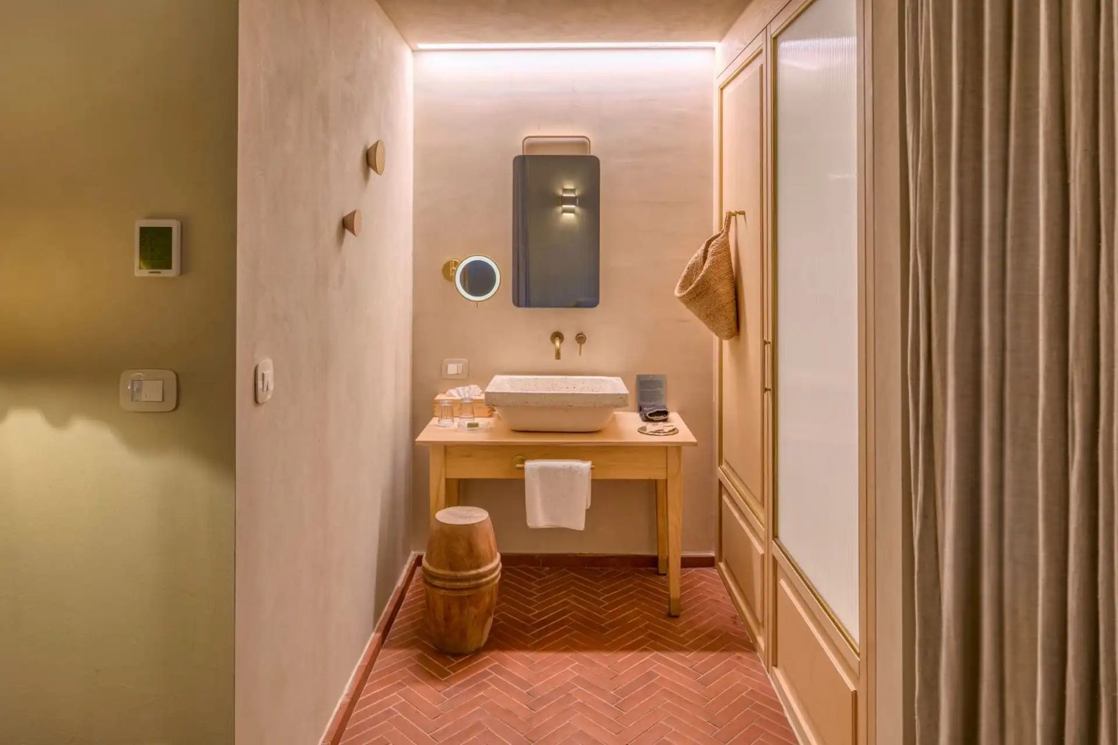 Badezimmer mit Holzwaschtisch, beleuchtetem Spiegel und rotem Fischgrätmuster am Boden.