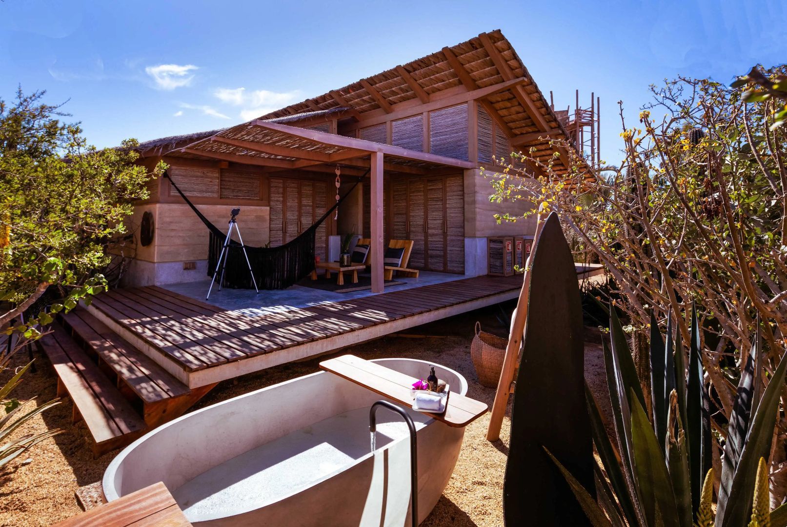 Holzhütte mit überdachter Terrasse, Hängematte und einer Badewanne im Freien.