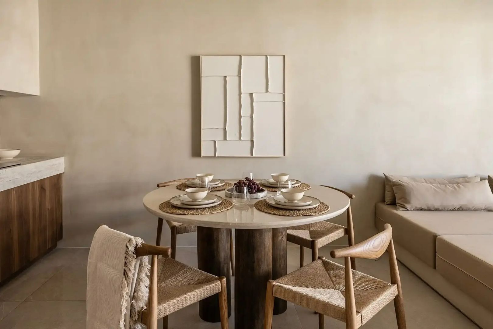 Esstisch aus Naturstein mit vier Holzstühlen vor einer beigen Wand mit Reliefkunst.