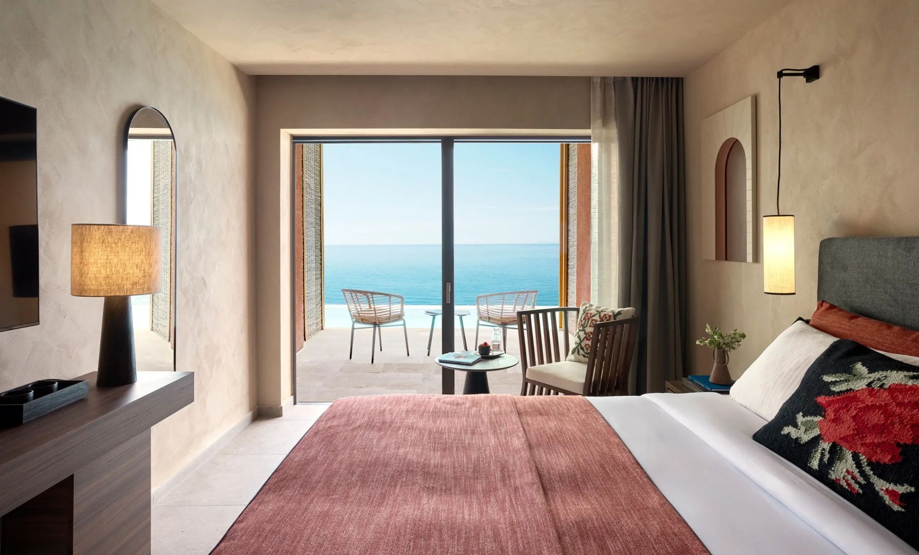 Blick aus dem Hotelzimmer mit Doppelbett auf Terrasse und das darunter liegende Meer.