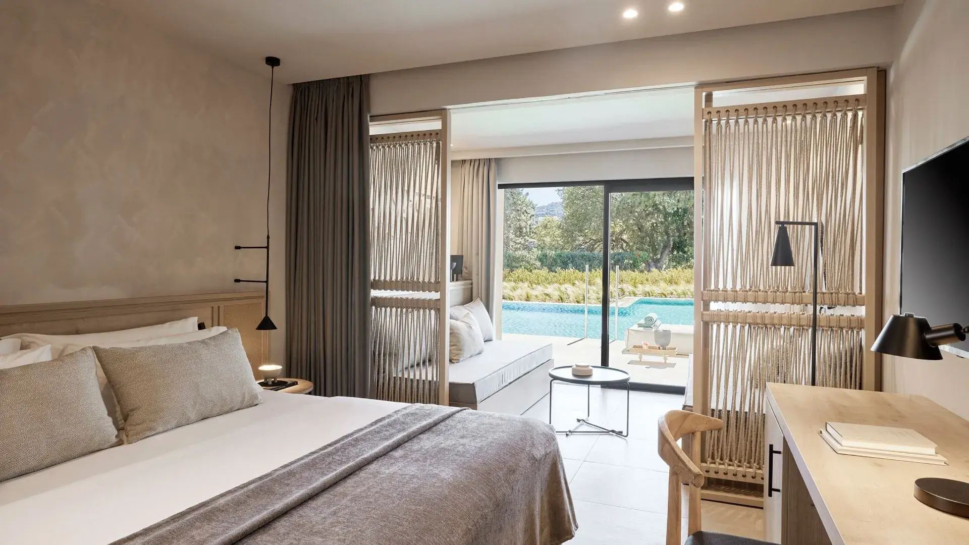Helles Hotelzimmer mit Doppelbett, Raumteiler aus Holz, Sitzbereich und Zugang zur Poolterrasse.
