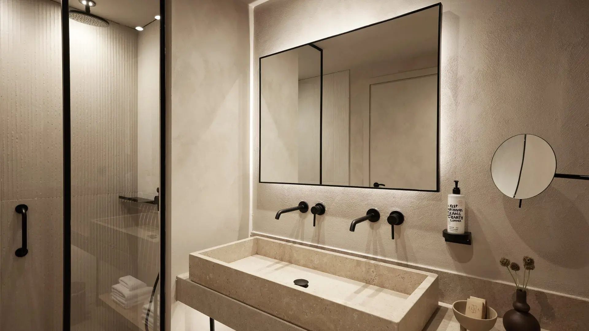 Badezimmer mit einem rechteckigen Steinwaschbecken, schwarzen Armaturen und großem Wandspiegel.