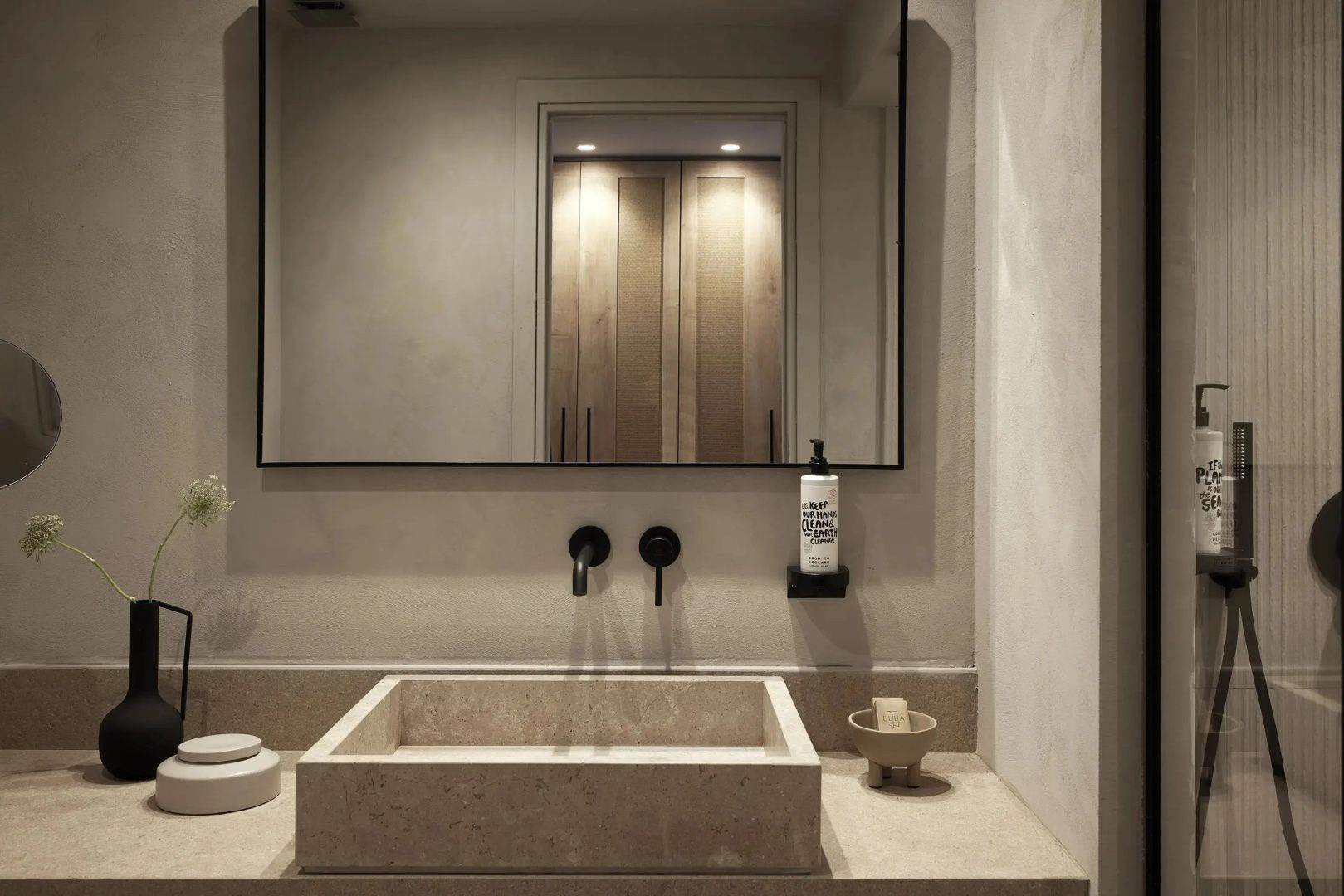 Modernes Badezimmer mit steinernem Waschbecken, schwarzer Armatur und Spiegel.