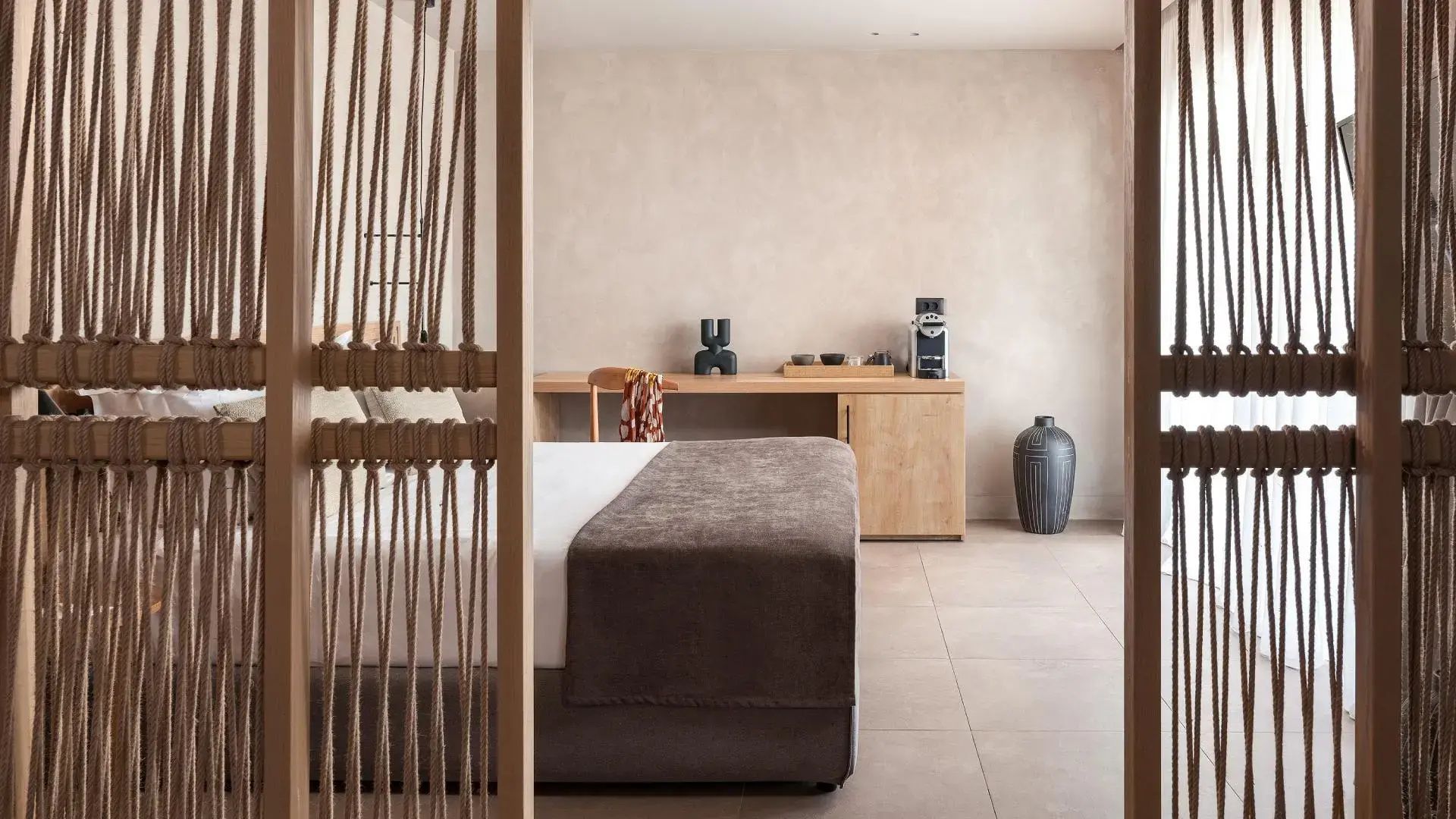 Hotelzimmer mit Doppelbett, Raumteiler aus Kordeln und einer Kommode aus Holz mit Kaffeemaschine.