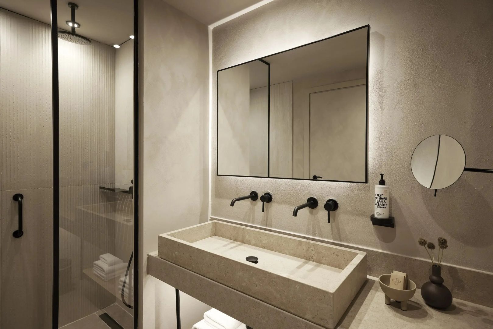 Modernes Badezimmer mit breitem Steinwaschbecken, schwarzen Armaturen und Wandspiegel.