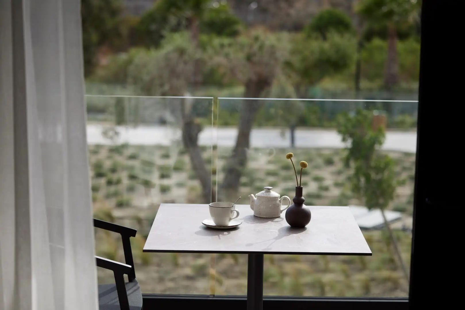 Balkontisch mit Kaffeetasse und kleiner Vase vor Glasbrüstung mit Blick ins Grüne.