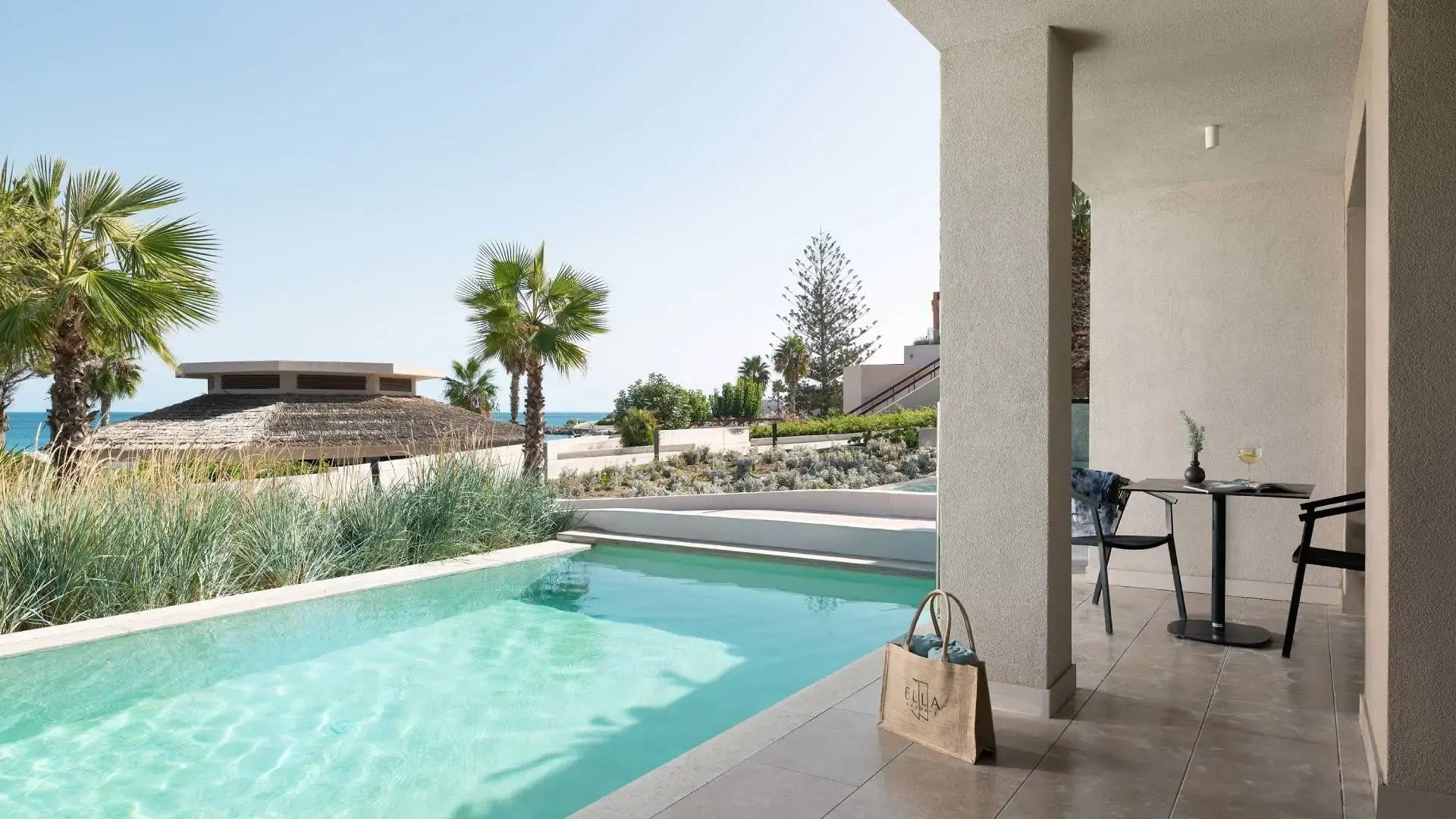 Privater Pool auf einer Terrasse mit Strandtasche und Blick auf Palmen und das Meer.