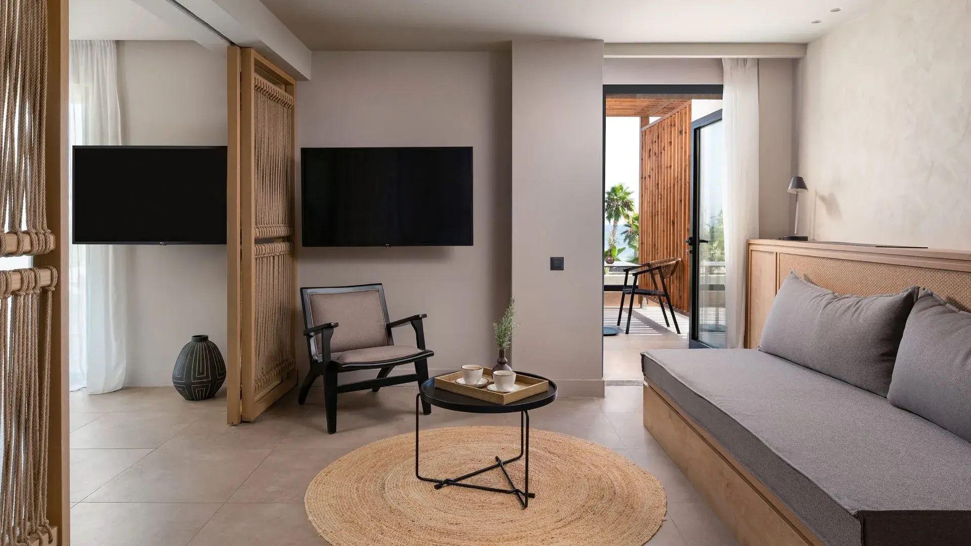 Helles Hotelzimmer mit Sessel, Wandfernseher und Zugang zur privaten Terrasse.