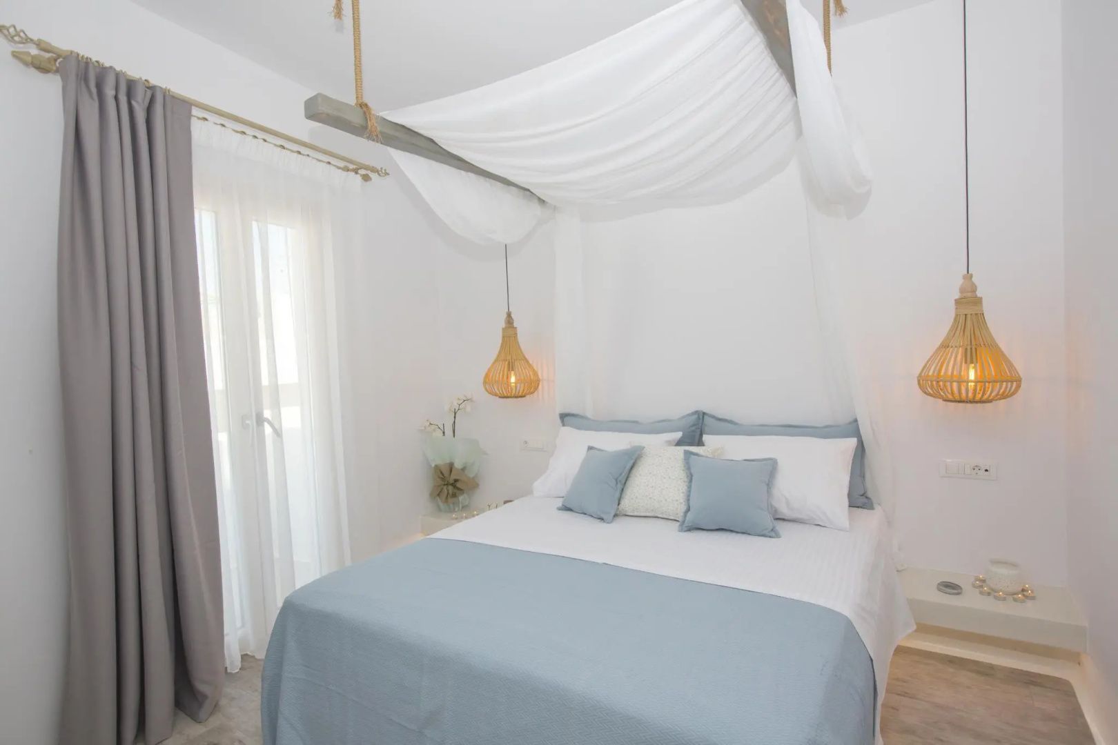 Hell eingerichtetes Schlafzimmer mit Doppelbett, weißem Himmelbaldachin und hellblauen Kissen.