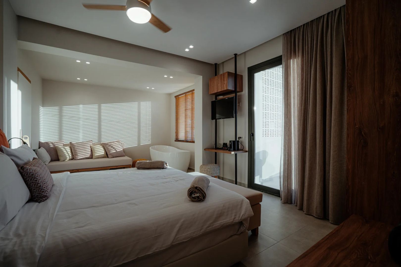 Modernes Hotelzimmer mit Doppelbett, beige-brauner Dekoration und einer freistehenden Badewanne.