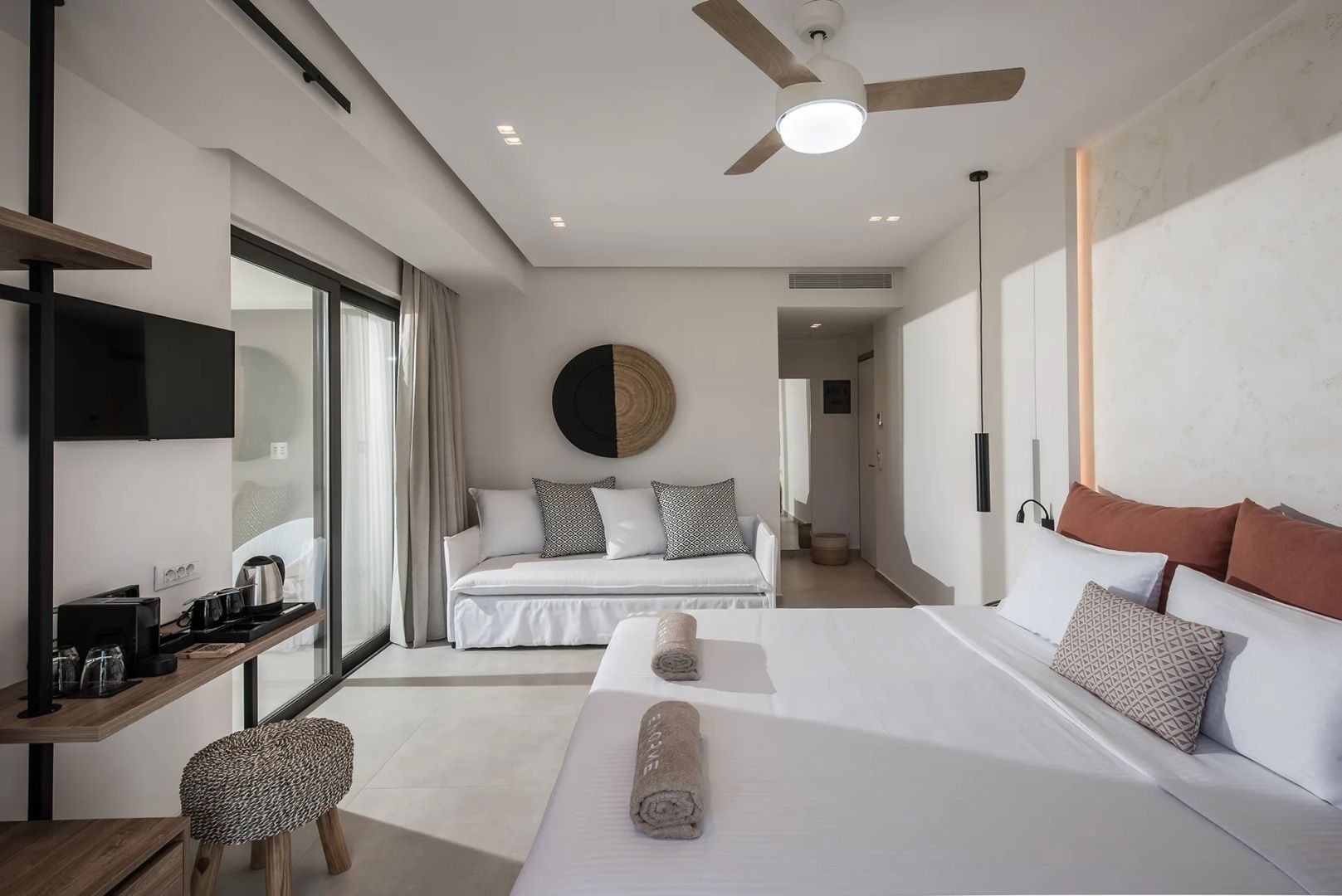 Modern eingerichtetes Hotelzimmer mit Doppelbett, weißem Sofa und Zugang zum Balkon.