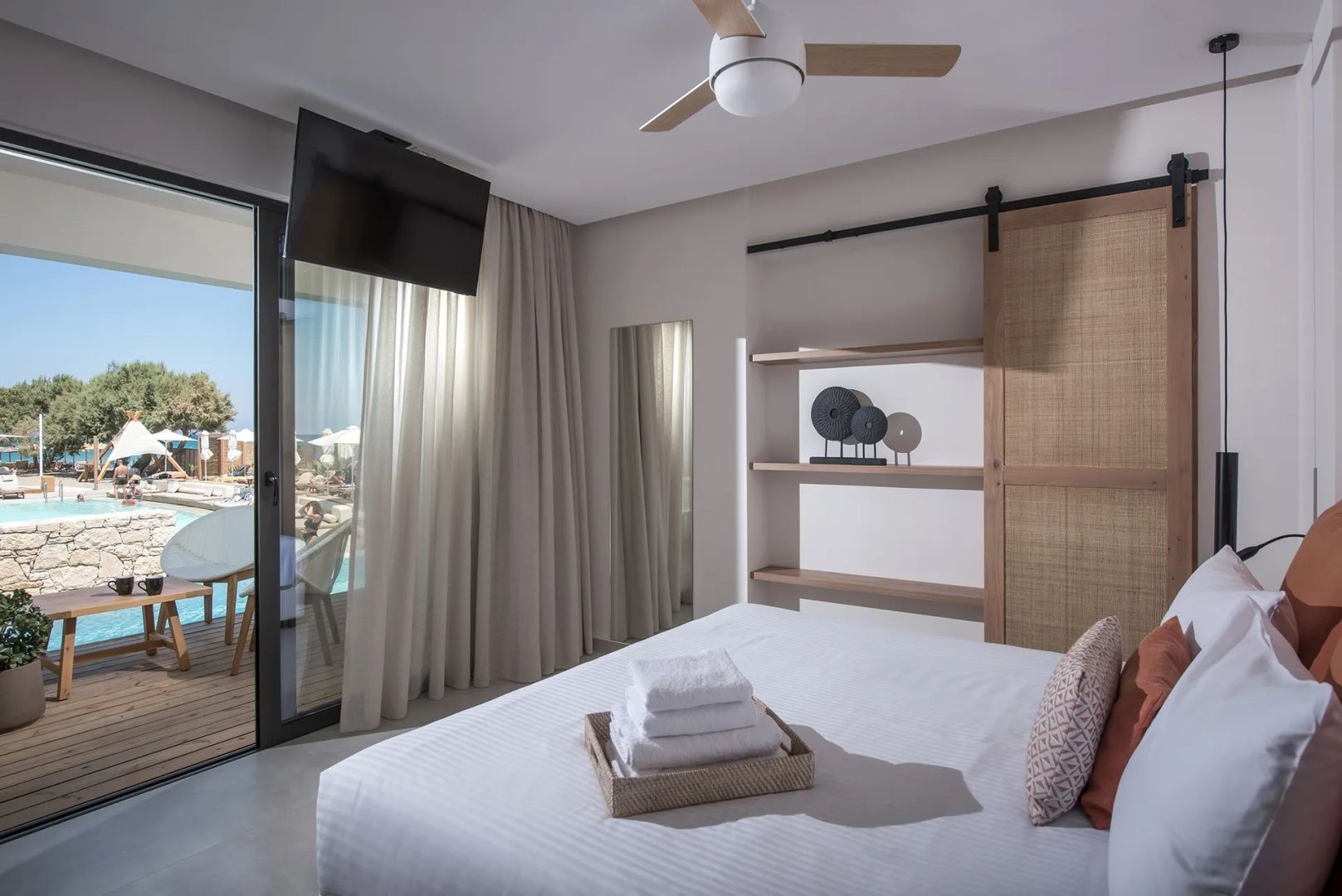 Doppelbett mit weißen Handtüchern, Deckenventilator und großem Balkonzugang.