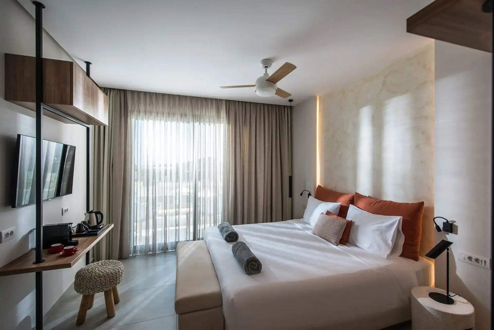 Hotelzimmer mit einem Doppelbett, warmen Farben, hellen Vorhängen und einem Deckenventilator.