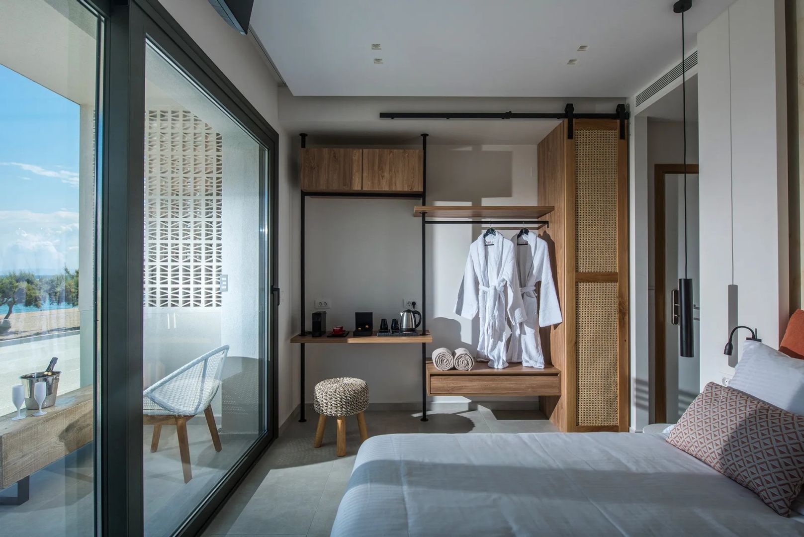 Offener Kleiderschrank aus Holz mit zwei weißen Bademänteln und einer kleinen Kaffeeecke im Hotelzimmer.