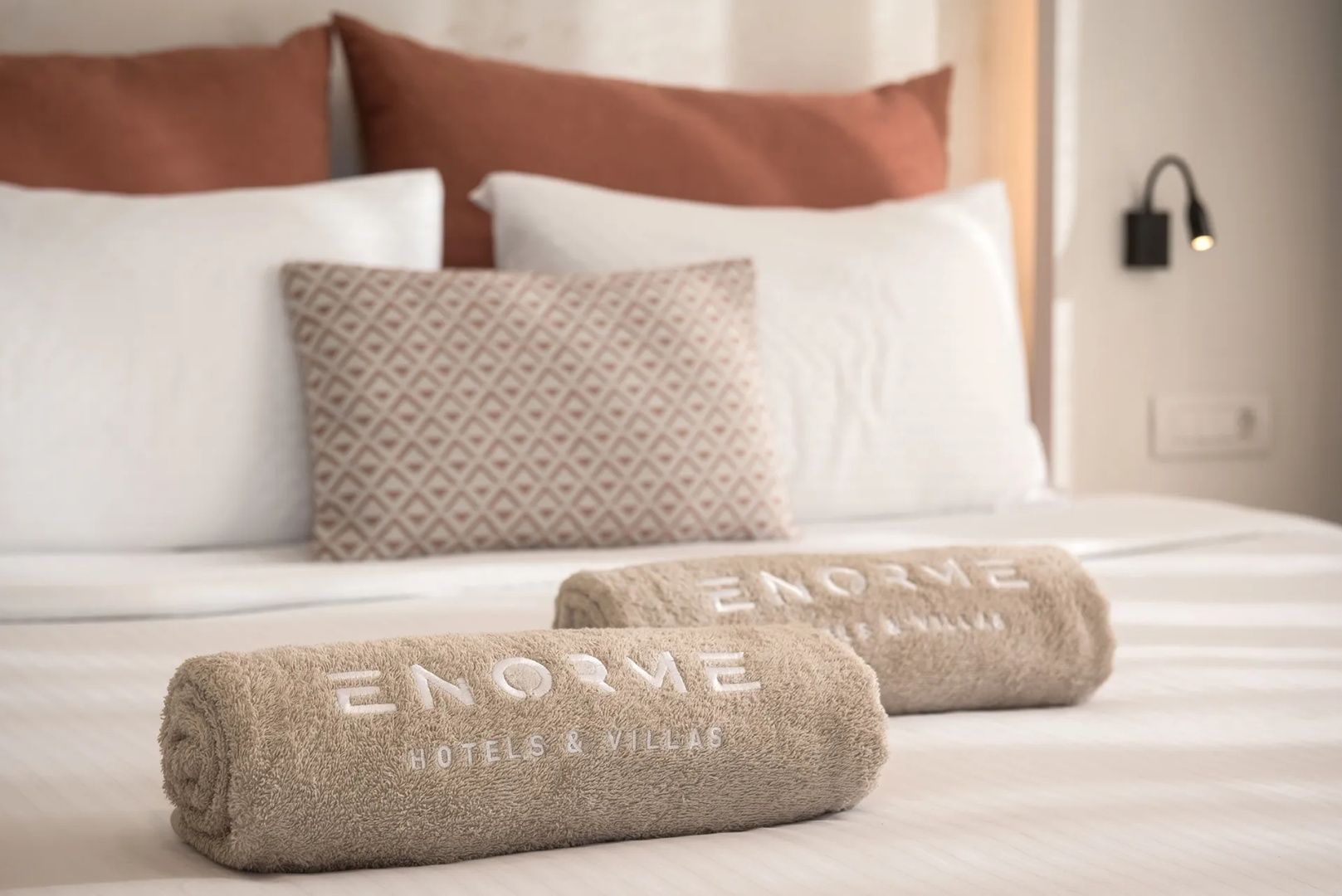 Zwei eingerollte beigefarbene Handtücher mit Stickerei auf einem gemachten Bett.