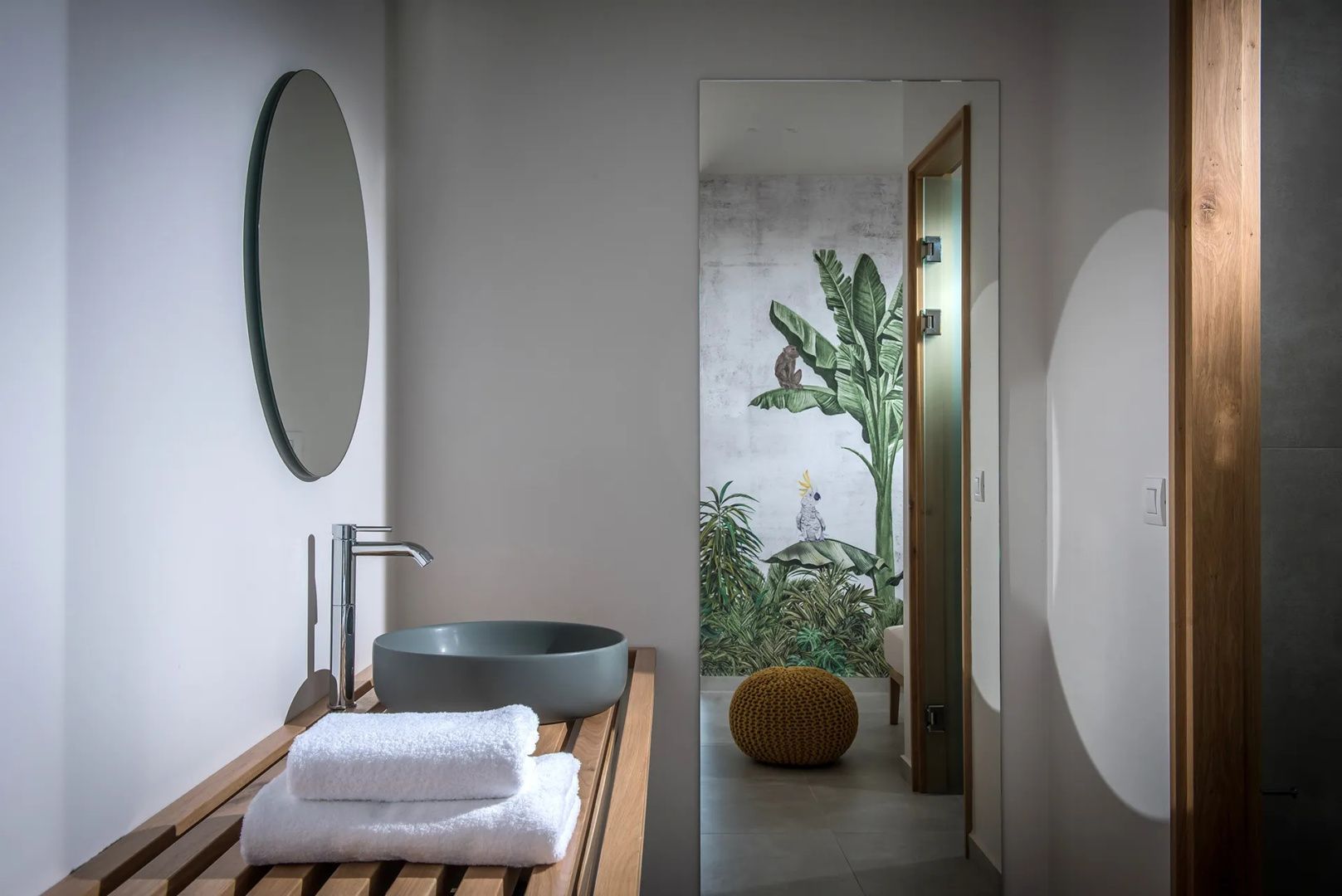 Badezimmer mit rundem Waschbecken auf Holztisch, Spiegel und Handtüchern.