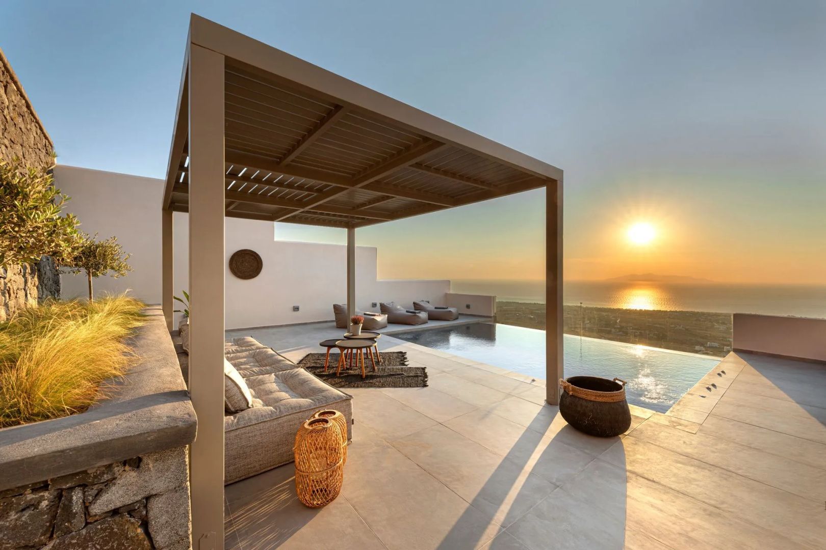 Terrasse mit Überdachung, Sitzmöbeln und Infinity-Pool bei Sonnenuntergang über dem Meer.