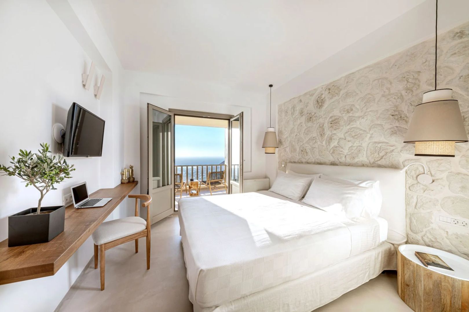 Helles Schlafzimmer mit Doppelbett, hölzernem Schreibtisch und Balkon mit Blick auf das Meer.