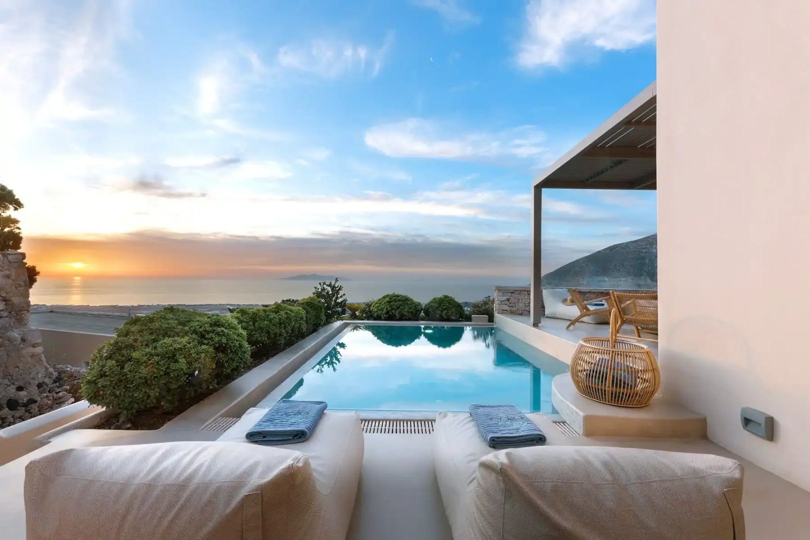 Privater Außenpool auf einer Terrasse mit Liegekissen und Blick auf das Meer bei Abenddämmerung.