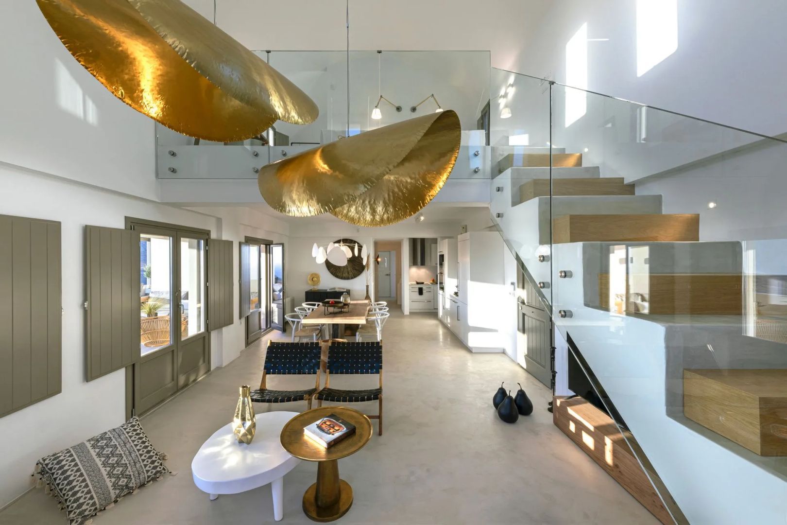 Offener Wohnbereich einer Villa mit Treppe, goldenen Hängelampen und Blick auf den Essbereich.
