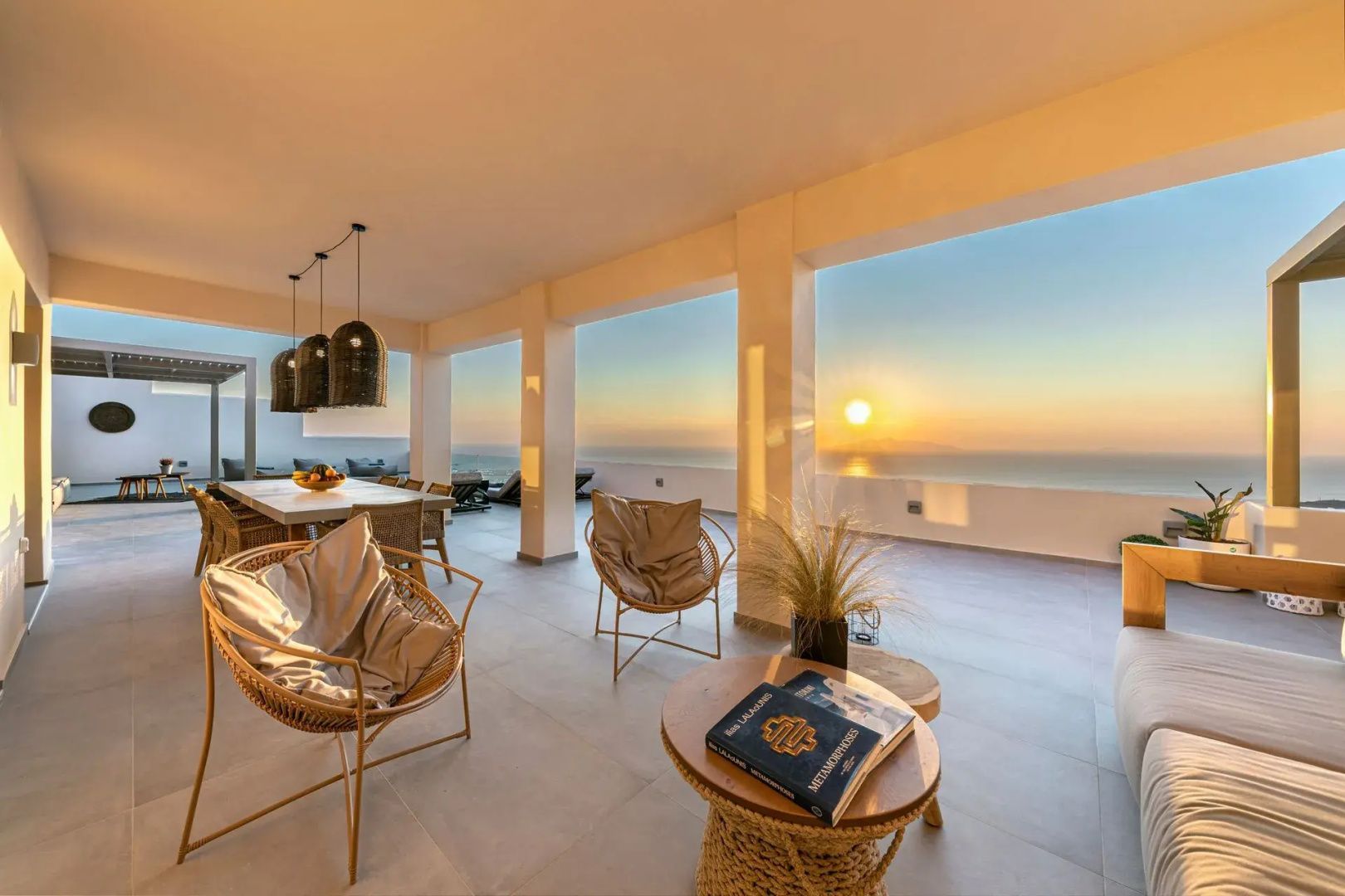 Überdachte Terrasse mit Sesseln und Blick auf das Meer bei Sonnenuntergang.