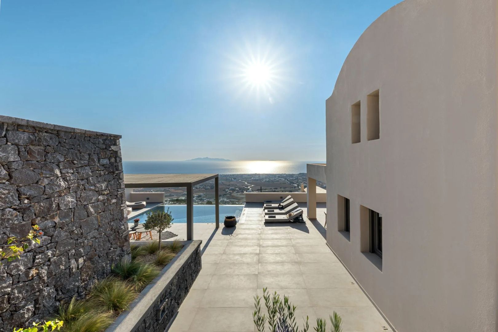 Außenbereich der Villa mit Steinmauern, Liegestühlen und Terrasse bei Sonnenschein.