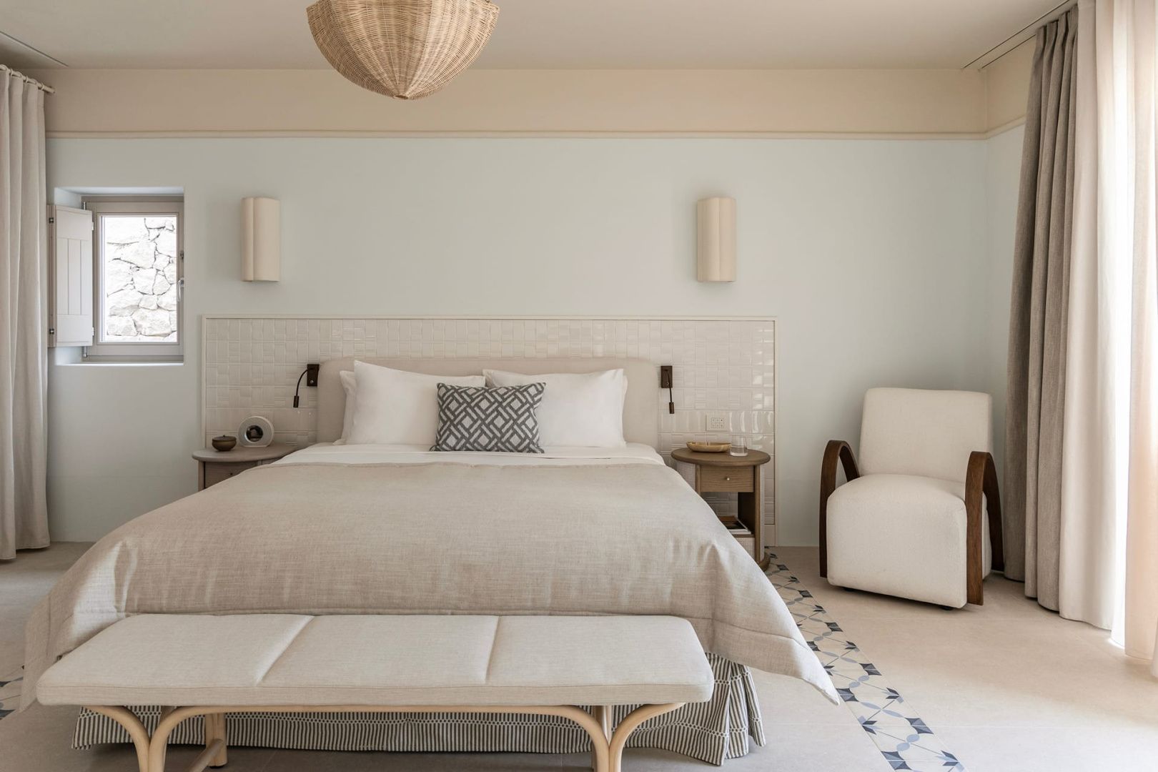 Doppelbett mit hellem Bezug, Bank davor und Sessel in beige eingerichtetem Zimmer