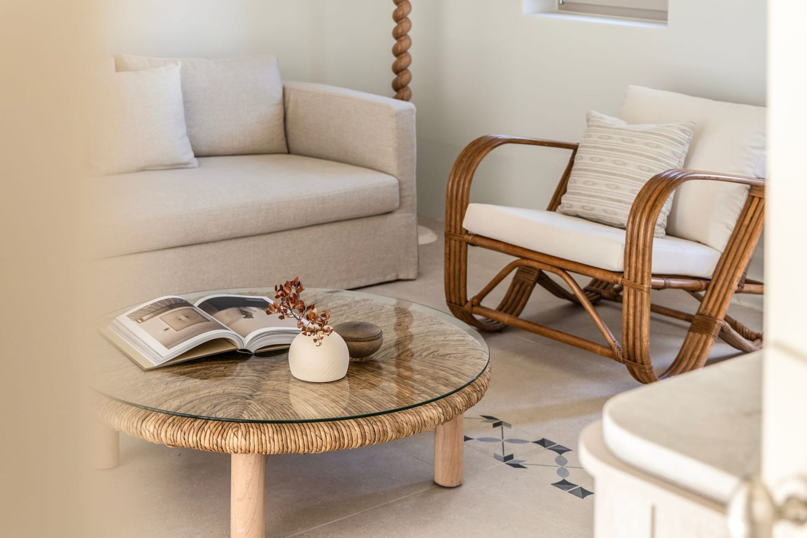 Sitzecke mit hellbeigem Sofa, Rattansessel und einem runden Couchtisch.