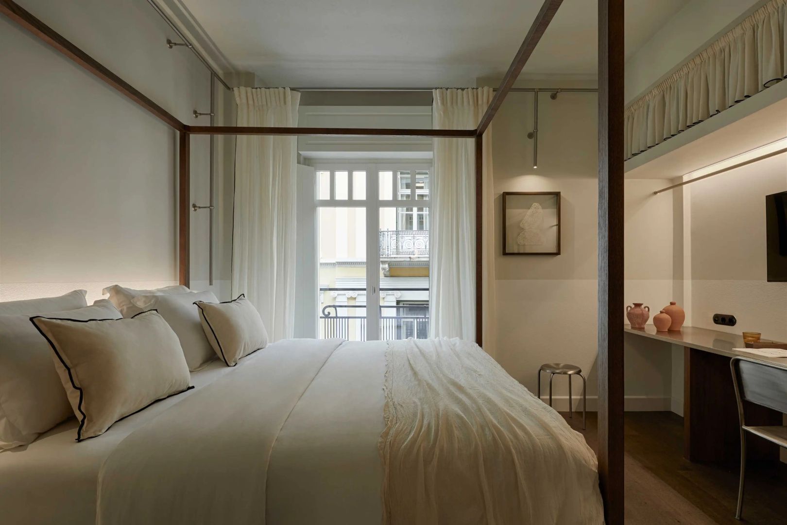 Helles Hotelzimmer mit einem hölzernen Himmelbett, weißen Kissen und Blick durch das Fenster.