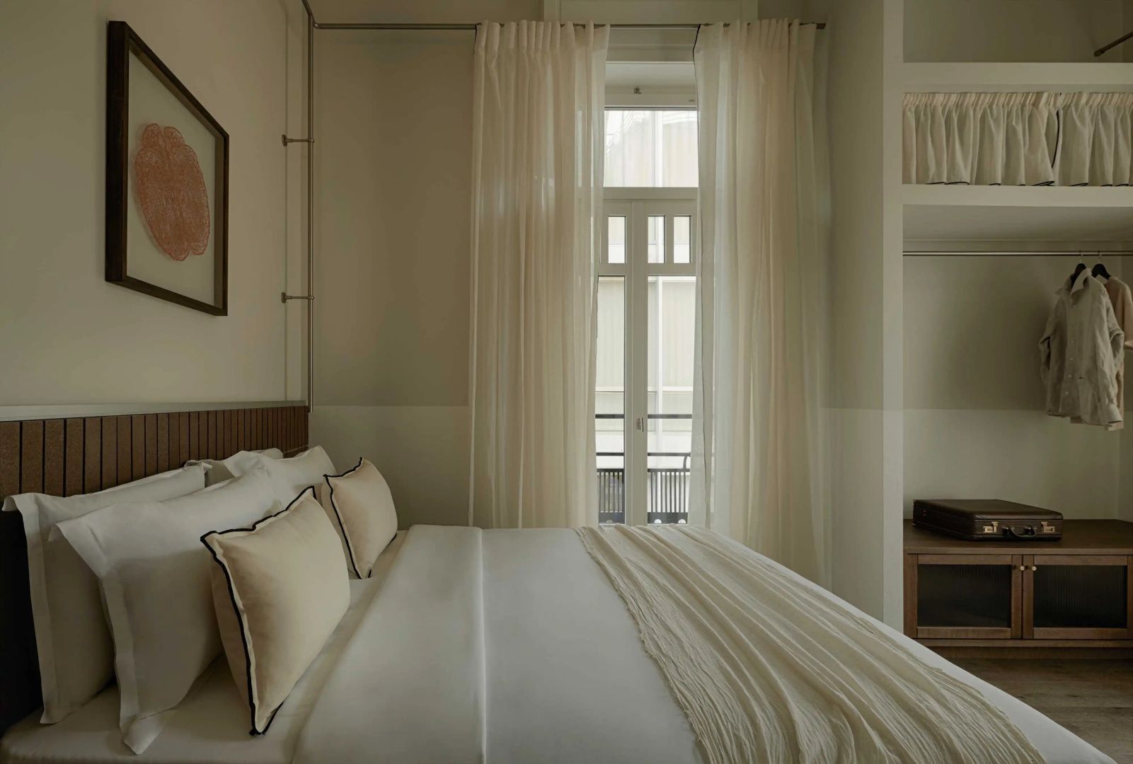 Blick über das Bett hin zu den hohen Fenstern mit Vorhängen und Balkontür.
