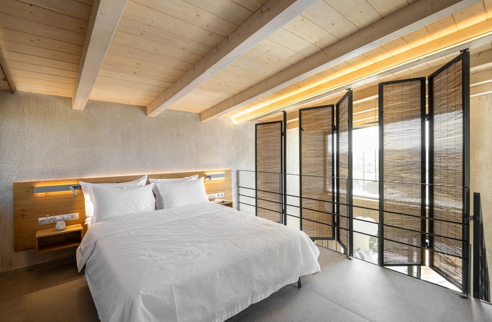 Doppelbett unter einer Holzdecke mit einem Raumteiler aus Naturmaterialien.
