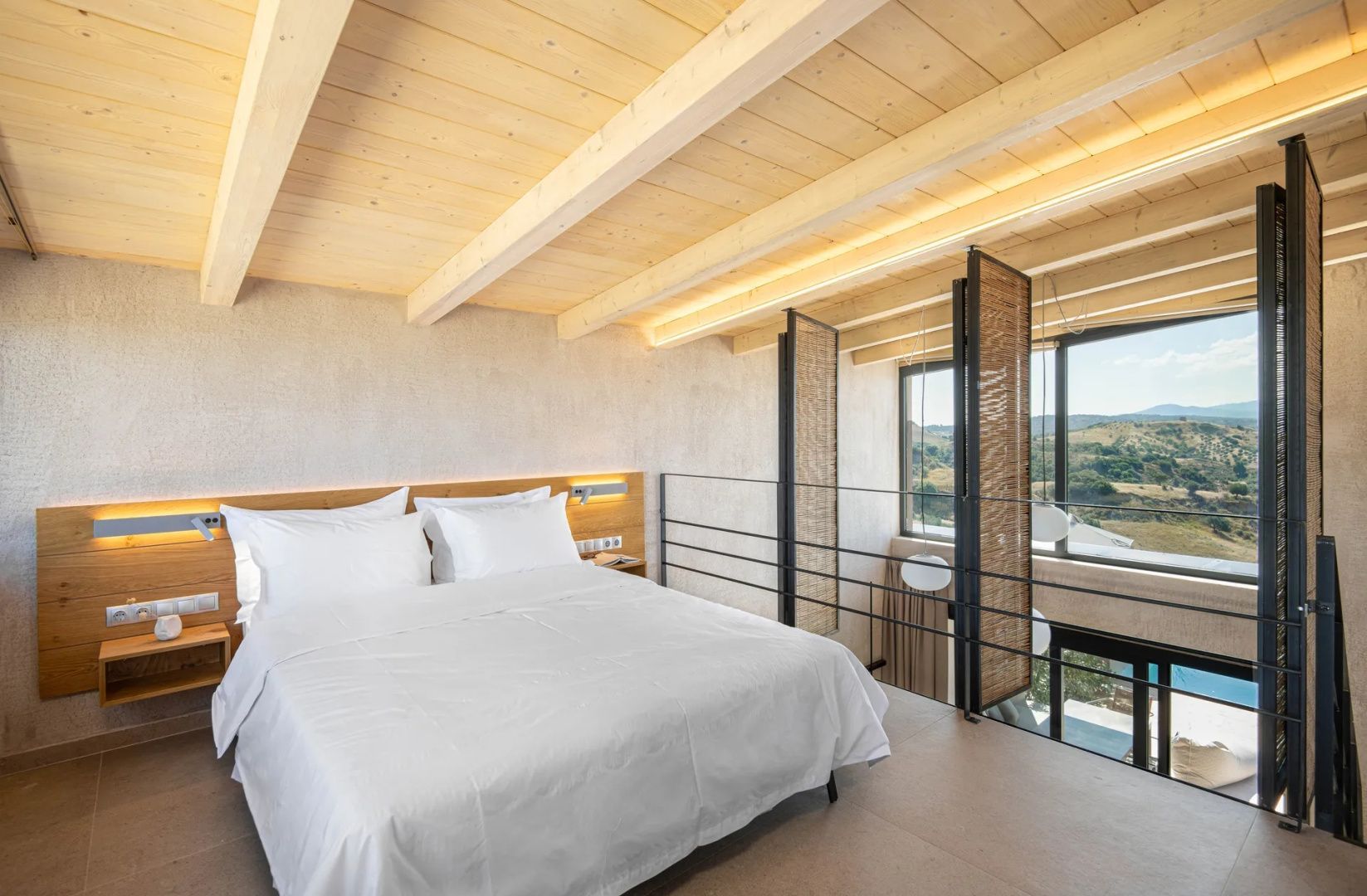 Helles Schlafzimmer auf einer Galerie mit Holzdecke und weiß bezogenem Doppelbett.