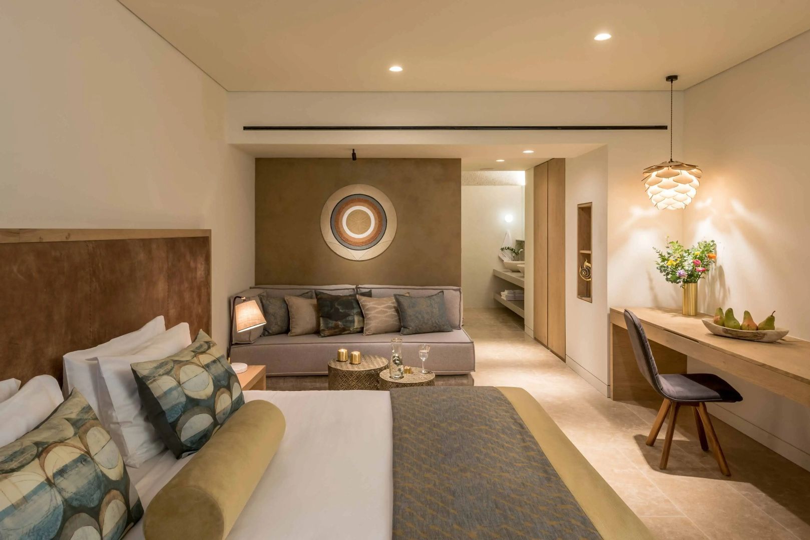 Hotelzimmer mit Doppelbett im Vordergrund, Sofa, Beistelltischen und Schreibtisch.