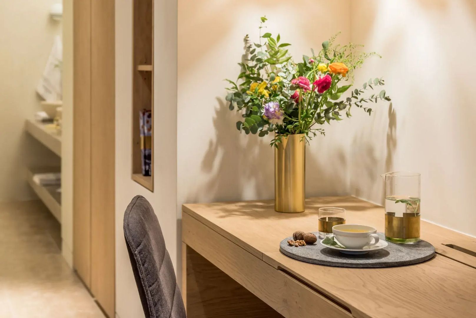 Arbeitsbereich im Hotelzimmer mit Holzschreibtisch, Stuhl und frischen Blumen.