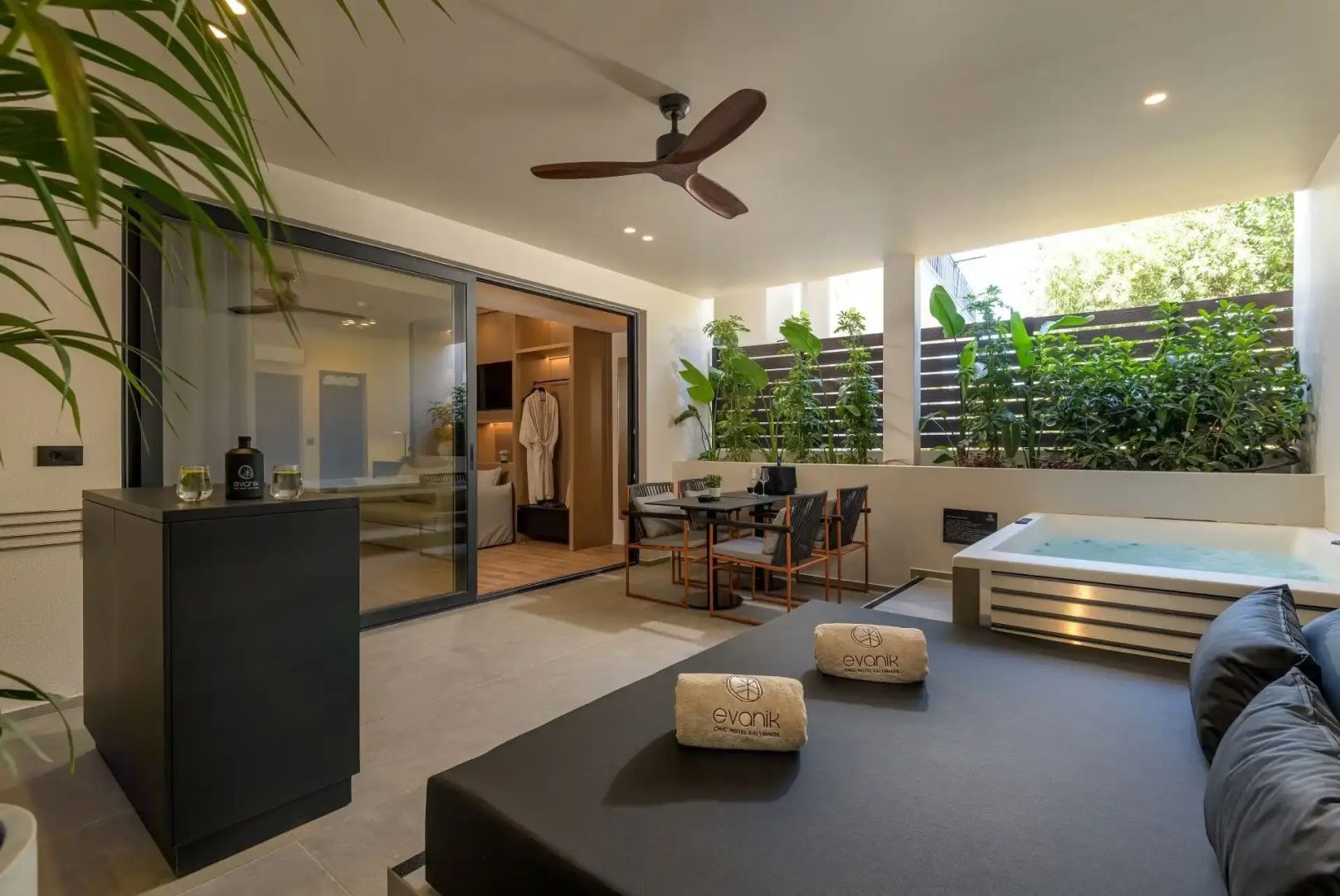 Überdachte Terrasse mit Jacuzzi, Sonnenliege, Sitzgruppe und Pflanzen vor dem Zimmer.