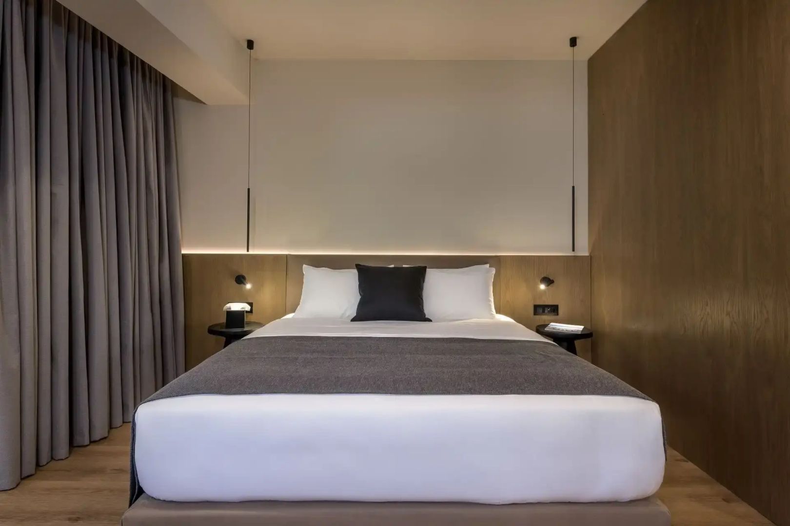 Doppelbett mit weißer Bettwäsche, grauem Überwurf und moderner Holzverkleidung.