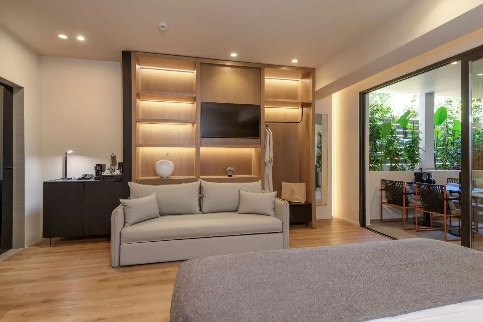 Moderner Wohnbereich im Hotelzimmer mit Sofa, Holzregal und Blick auf die Terrasse.