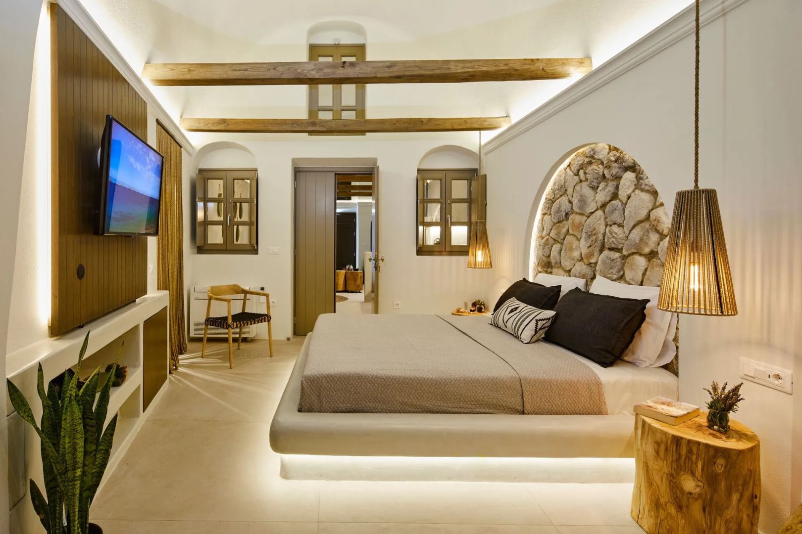 Doppelbett mit beleuchtetem Stein-Kopfteil und Holzbalken an der Decke in einer hellen Suite.