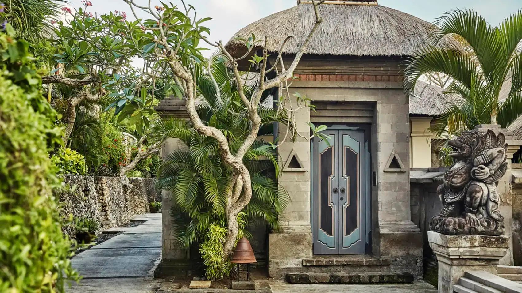 Eingangsbereich einer Villa mit traditionellem Reetdach, verzierter Tür und tropischen Pflanzen.