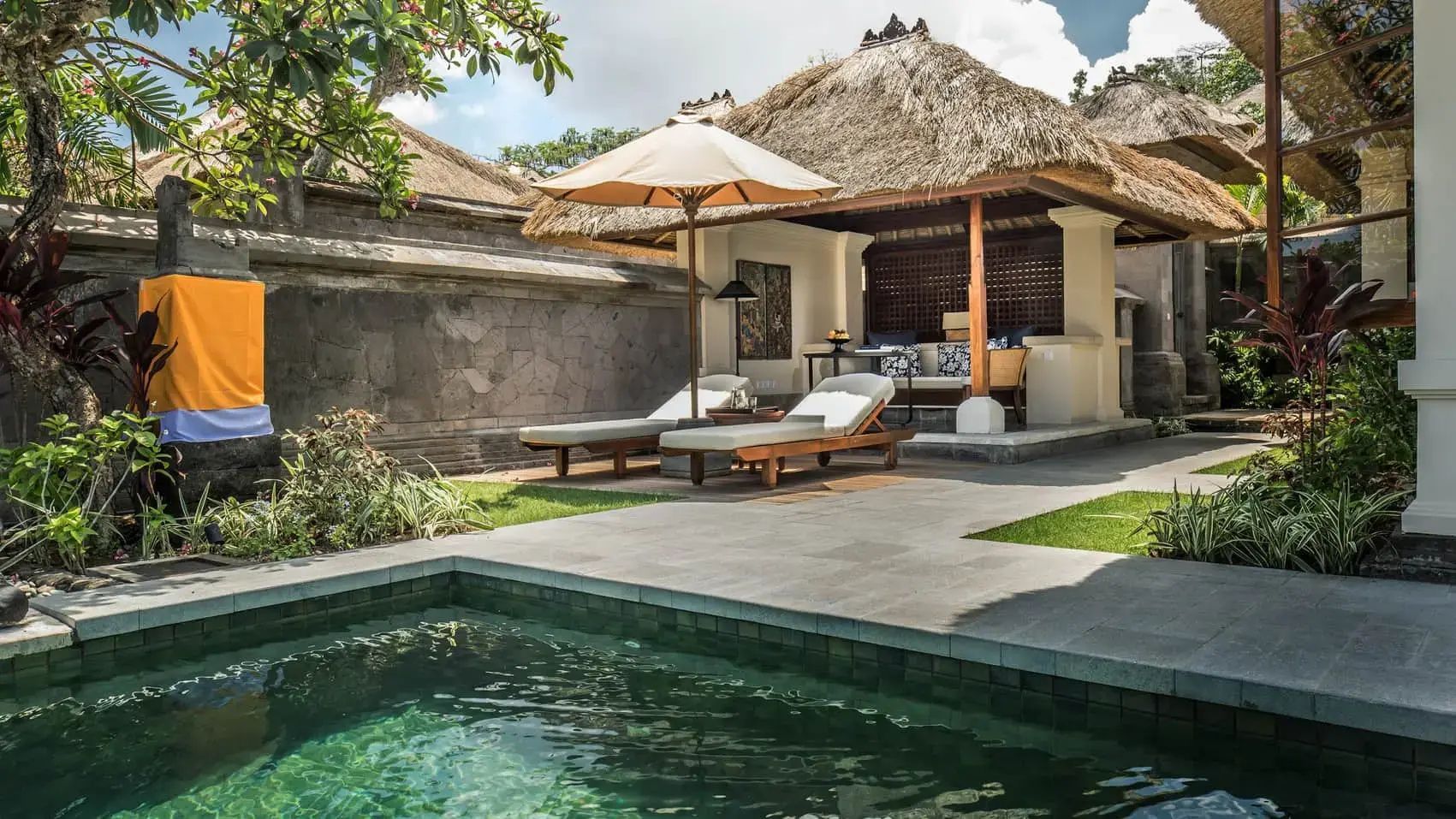 Privater Poolbereich einer Villa mit Sonnenliegen, Schirm und reetgedeckter Überdachung.