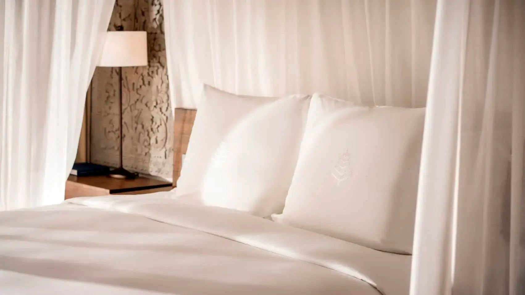 Nahaufnahme von weißer Bettwäsche und Kissen auf einem Doppelbett im Hotelzimmer.