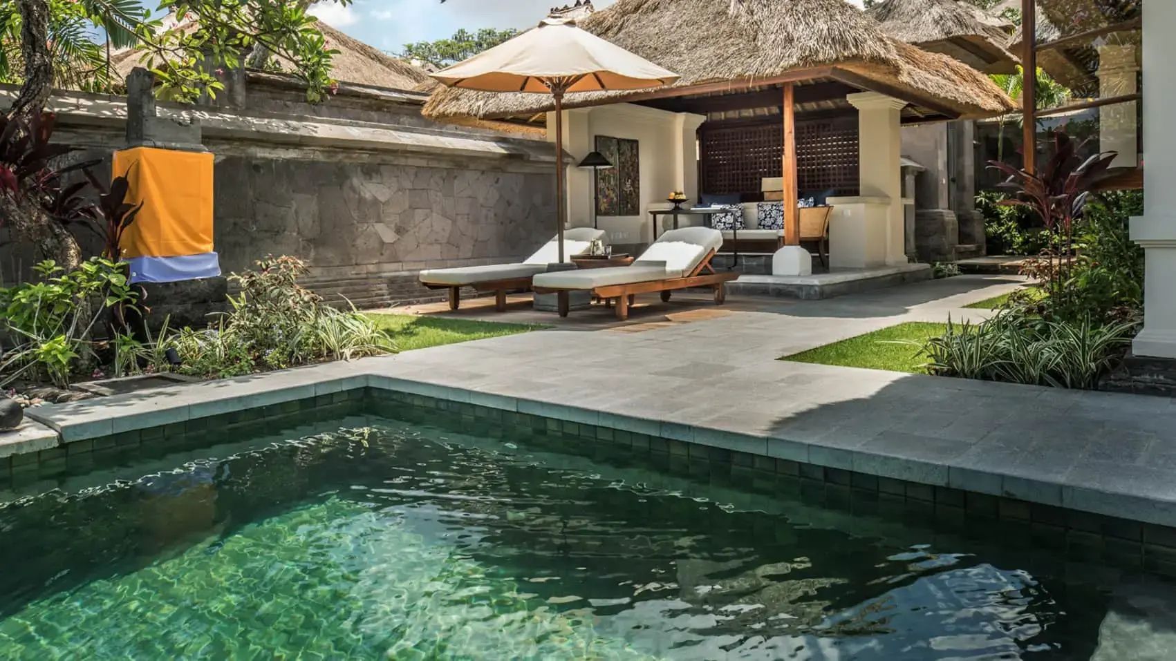 Poolbereich einer Villa mit zwei Holzliegen unter einem Schirm und Pavillon.