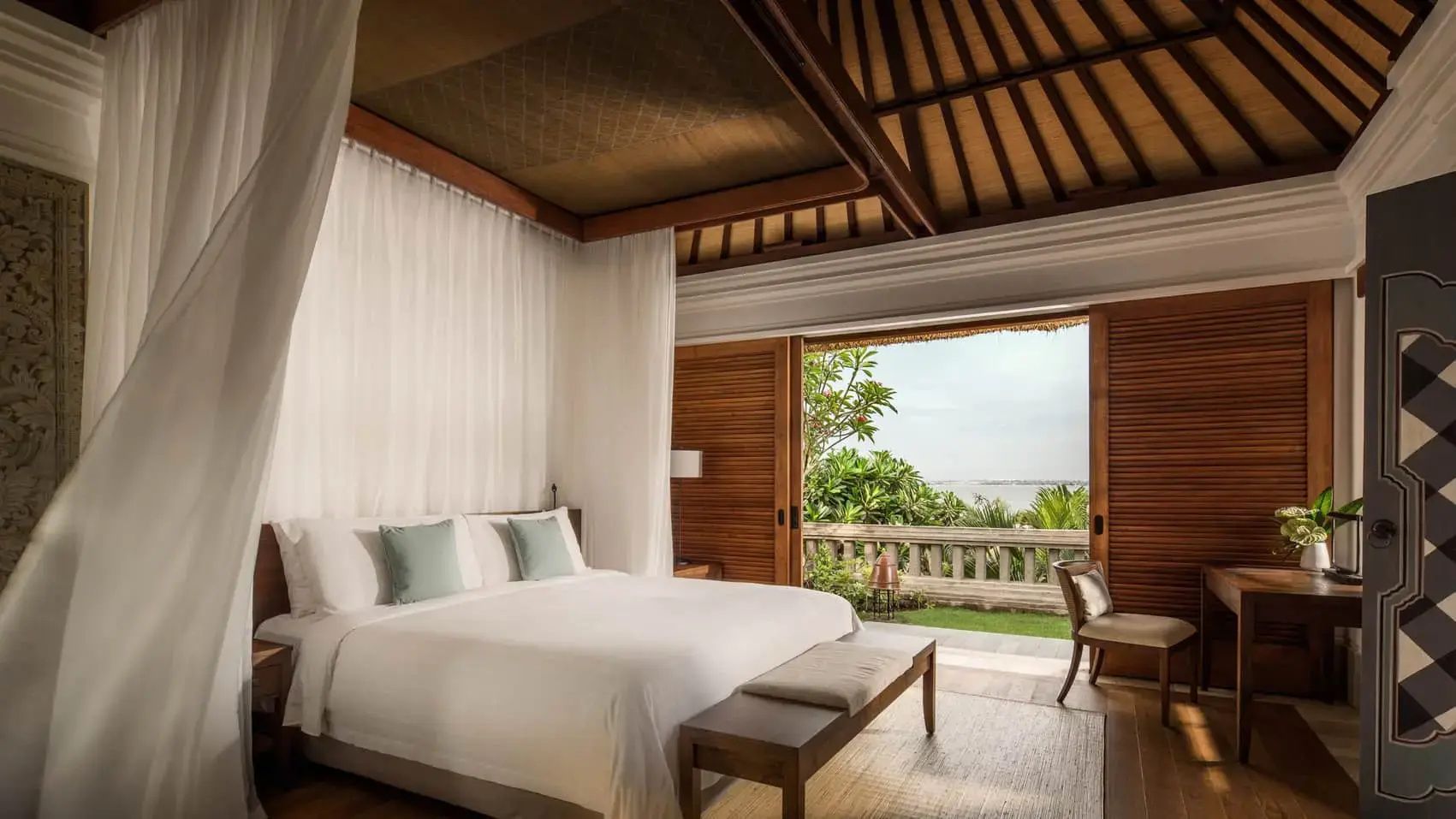 Helles Schlafzimmer einer Villa mit Holzdecke, großem Doppelbett und Blick ins Grüne.