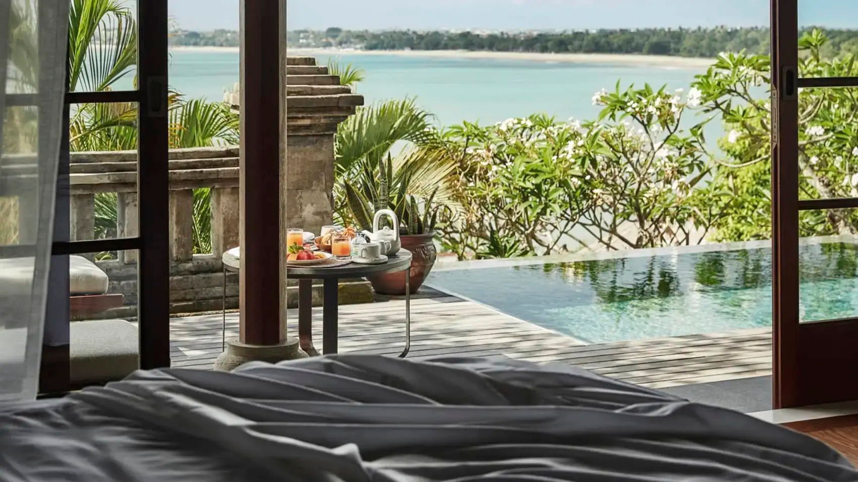 Terrassenbereich am Pool mit Frühstückstisch und Blick auf die Küste und das Meer.
