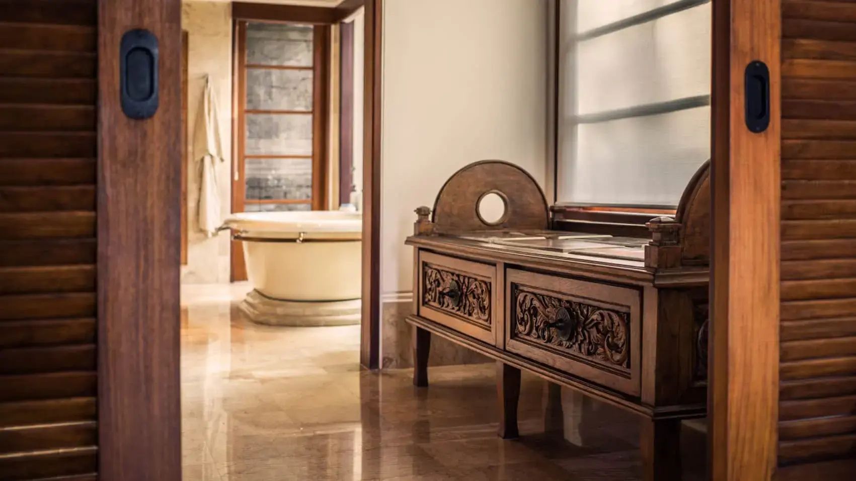 Holzschrank im Vorraum zu einem Badezimmer mit freistehender Badewanne.