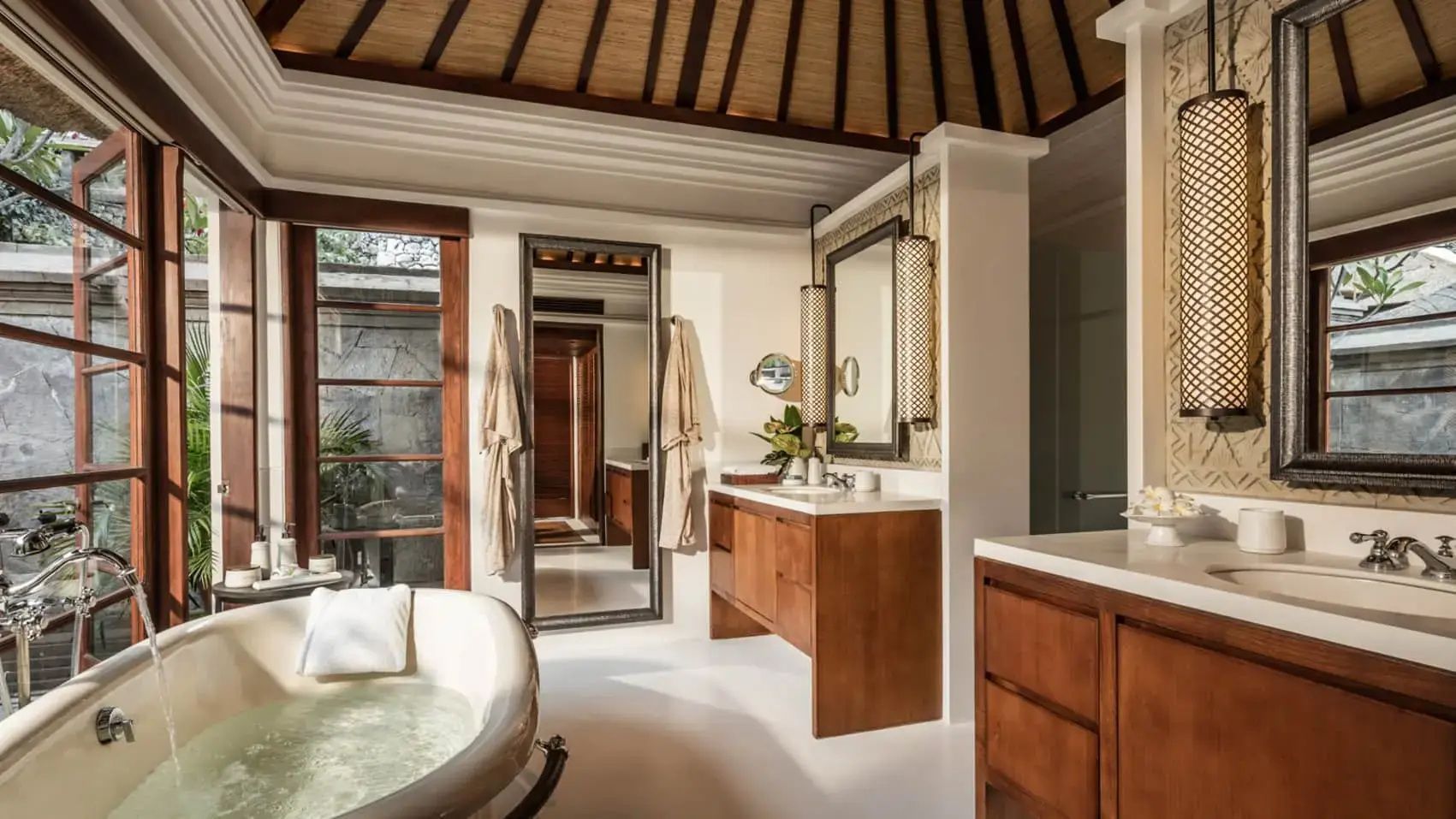 Badezimmer mit frei stehender Badewanne, Holzwaschtisch, großem Spiegel und Reetdach.