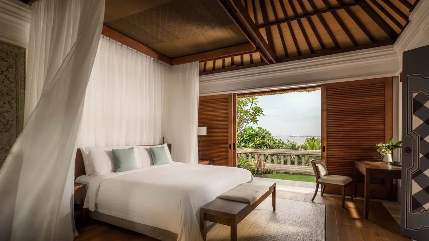 Schlafzimmer mit großem Bett und Blick durch geöffnete Flügeltüren auf die Terrasse und das Meer.