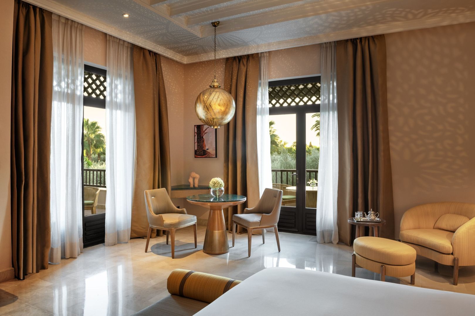 Sitzecke im Hotelzimmer mit zwei Sesseln, rundem Tisch und Hängeleuchte vor Balkontüren.