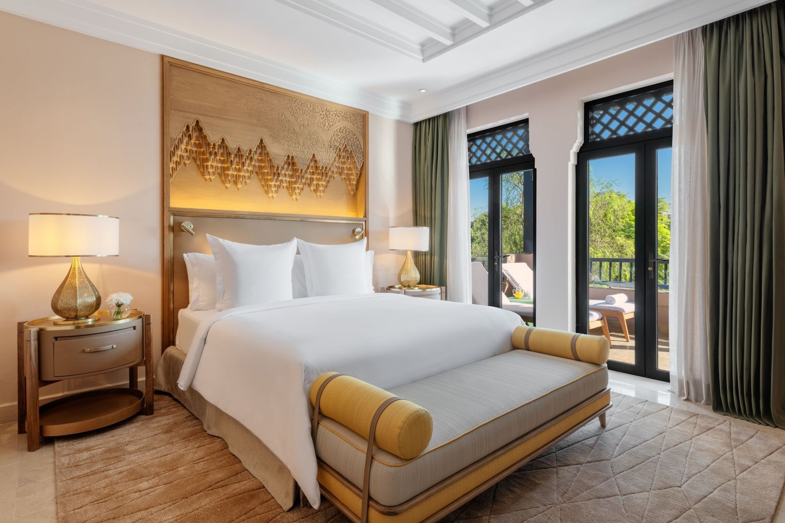 Helles Hotelzimmer mit Doppelbett, Sitzbank am Bettende und Blick auf den Balkon.