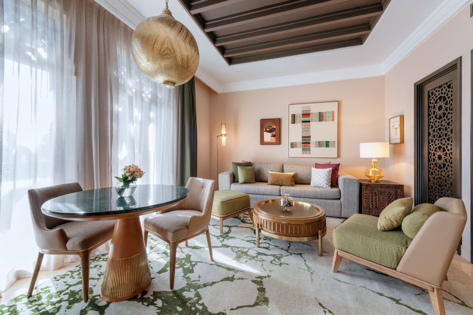 Wohnbereich einer Suite mit grauem Sofa, grünen Sesseln, Couchtisch und Teppich.